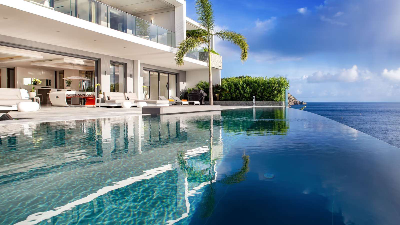A stunning aerial drone shot of a luxury villa's infinity pool seamlessly blending with the turquoise sea of Gouverneur.