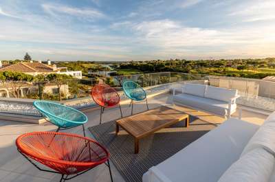 Stylish rooftop lounge featuring vibrant Acapulco chairs, sleek sofas, and panoramic Algarve golf and lake views.