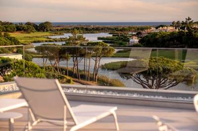 Glass-balustrade terrace offering panoramic views of the lush golf course, tranquil lake, and distant Atlantic Ocean.