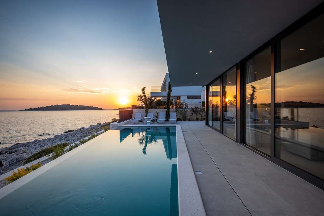 Sleek saltwater infinity pool reflecting a golden sunset over the Adriatic Sea at this modern luxury villa in Rogoznica.