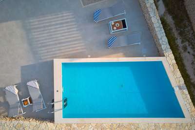 Aerial view of the pristine private pool and elegant sun loungers on the stone terrace of Adriatic Edge luxury villa.