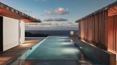 St-Barths luxury villa featuring an illuminated infinity pool, modern wood architecture, and breathtaking ocean views at dusk