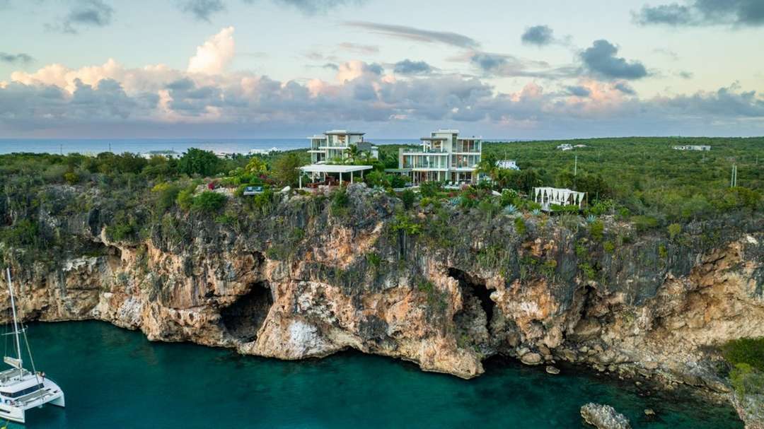 Aerial view of ÀNI Anguilla's contemporary villas perched on a rugged clifftop above Little Bay with Caribbean Sea views.