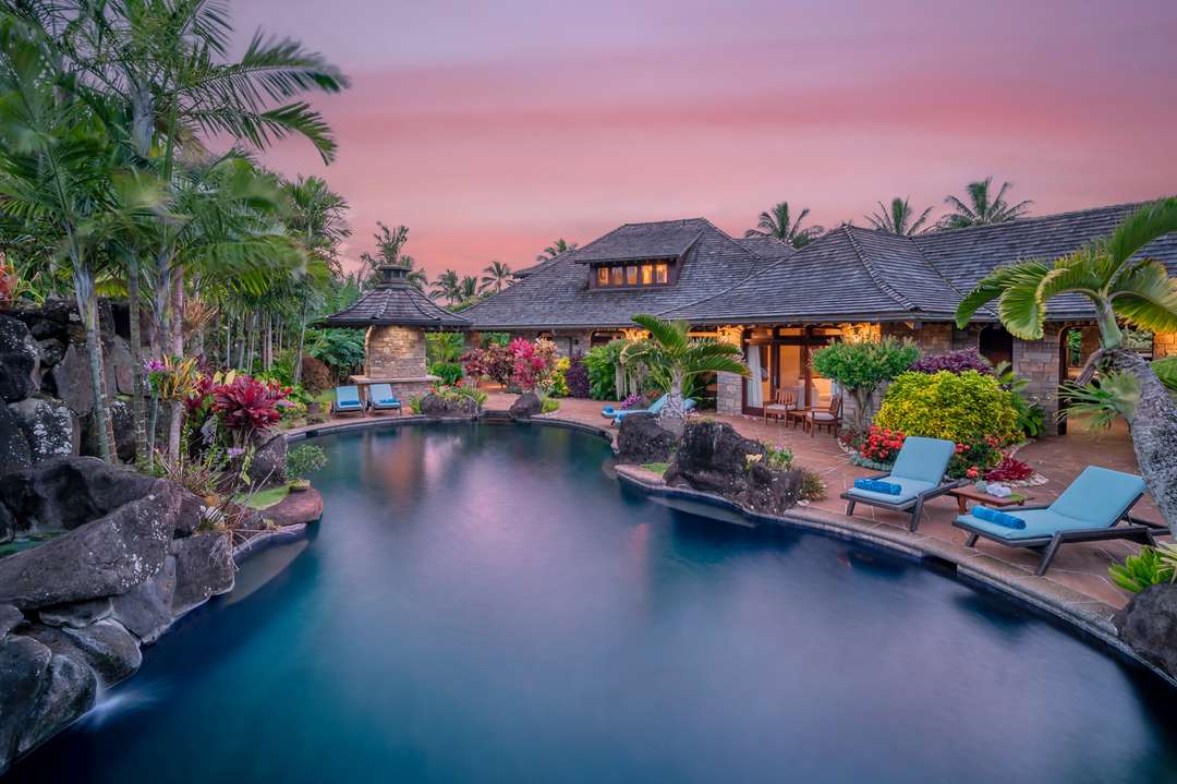 Lagoon-style saltwater pool at Anini Vista Drive Estate at sunset, featuring lush gardens and luxury stone villa in Kauai.