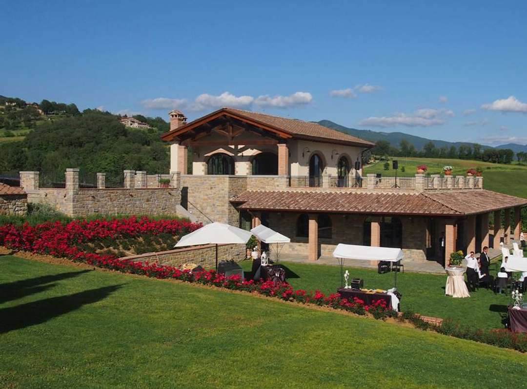 Elegant stone villa at Antico Estate featuring a lush lawn, vibrant red roses, and an outdoor event setup in Tuscany.