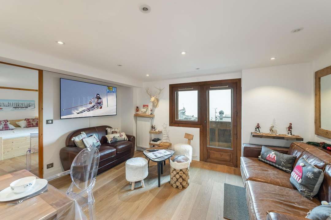 Elegant living area in Apartment Chamois 201 featuring a plush leather sofa, wooden floors, and balcony access in Courchevel.