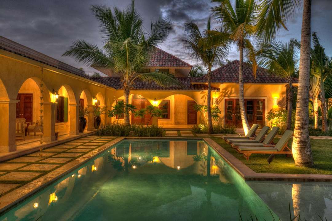Evening view of Arrecife 24's private pool in Punta Cana, featuring elegant arched walkways, palm trees, and warm lighting.