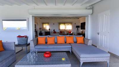 Expansive covered terrace featuring a chic grey wicker lounge area with vibrant orange accents and serene ocean views.