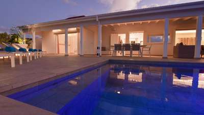 Inviting heated swimming pool glowing at night beside a grand covered terrace with chic lounge seating and dining space.