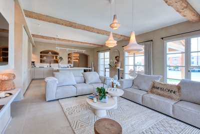 Elegant open-plan living room with plush sofas, rustic wooden beams, woven pendant lights, and scenic waterfront views.