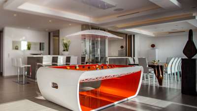 Modern living room featuring a lacquered orange pool table and an elegant dining area with a rich wood table seating ten.