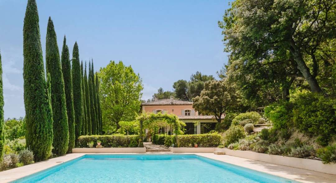 Private pool at Bastide Des Jardins, surrounded by tall cypress trees and lush Provençal gardens with the villa beyond.
