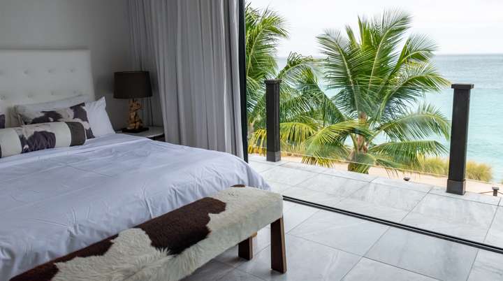 Elegant ground floor bedroom at Beach House 5 with a plush bed, marble floors, and a private terrace offering ocean views.