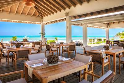 Open-air beachfront restaurant at Tamarind Hills featuring elegant wooden dining tables and panoramic Caribbean Sea views.
