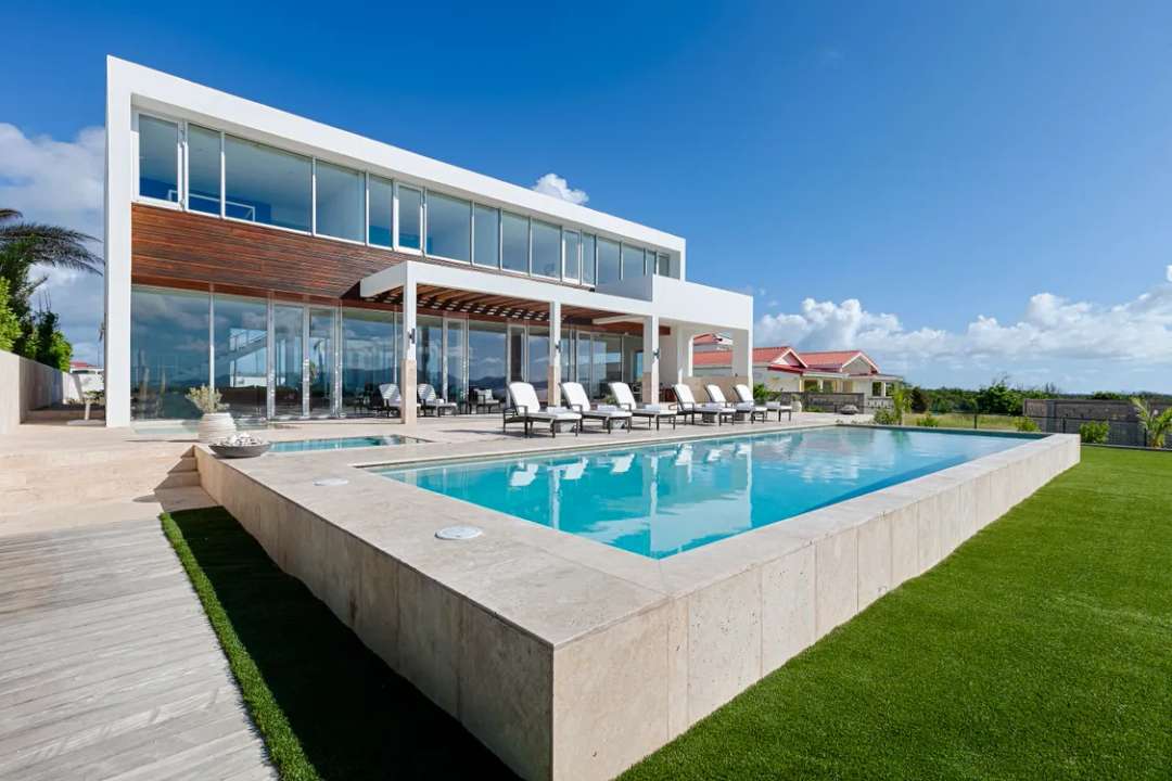 Modern minimalist Beaches Edge villa exterior featuring a sleek pool, stone terrace, and elegant wood architectural accents.