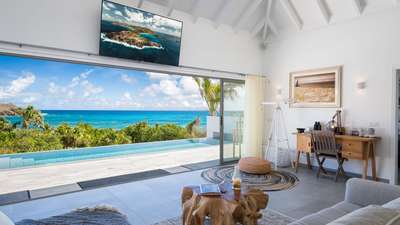 Elegant living area with plush seating, vaulted white ceilings, and expansive openings framing magnificent ocean vistas.