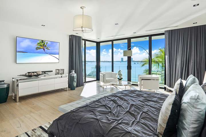 Luxury primary bedroom featuring a king bed, smart TV, and floor-to-ceiling windows with direct waterfront views in Miami.