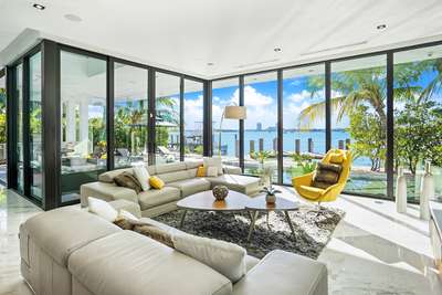 Contemporary living area featuring a plush sectional, marble floors, and panoramic waterfront views of North Bay Village.