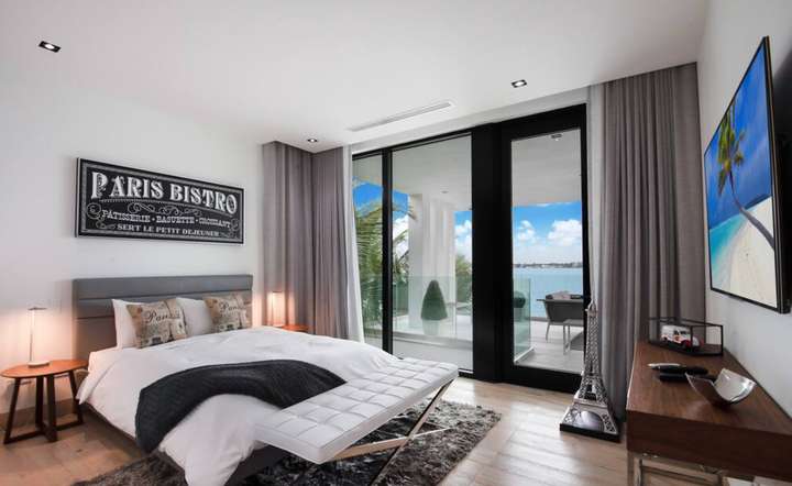 Paris-themed bedroom offering a king bed, elegant decor, and floor-to-ceiling windows opening to a waterfront balcony.