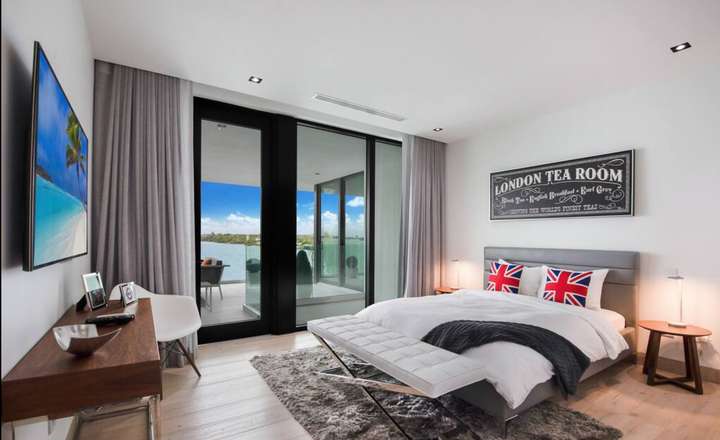 London-themed guest bedroom featuring a queen bed, modern furnishings, and private balcony access with stunning bay views.