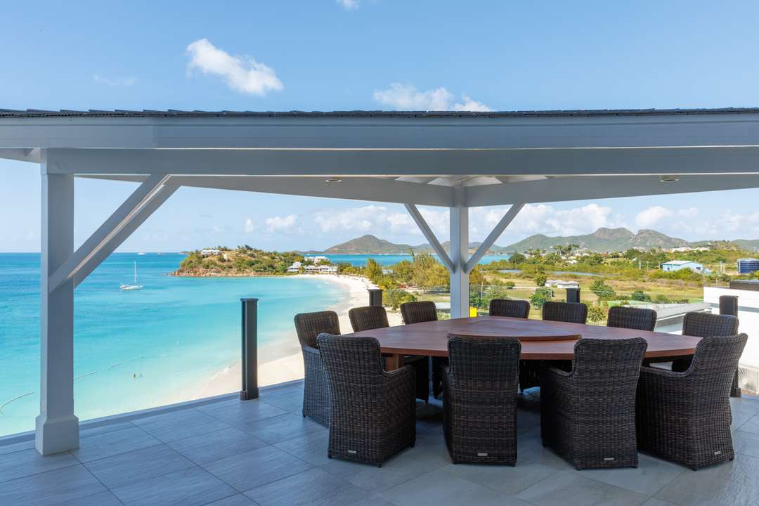Covered alfresco dining space at Blue Heaven Rendezvous featuring a round wooden table and panoramic Caribbean Sea views.