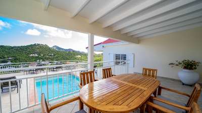 Generous covered terrace with an elegant wooden dining table seating six, overlooking the private pool and lush green hills.
