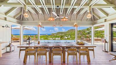 Luxury villa al fresco dining area featuring a large wooden table, vaulted ceilings, and panoramic St-Jean Bay ocean views.