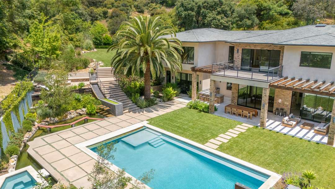 Aerial view of Bowmont villa's expansive backyard in Beverly Hills featuring a large private pool, lush lawn, and palm trees.