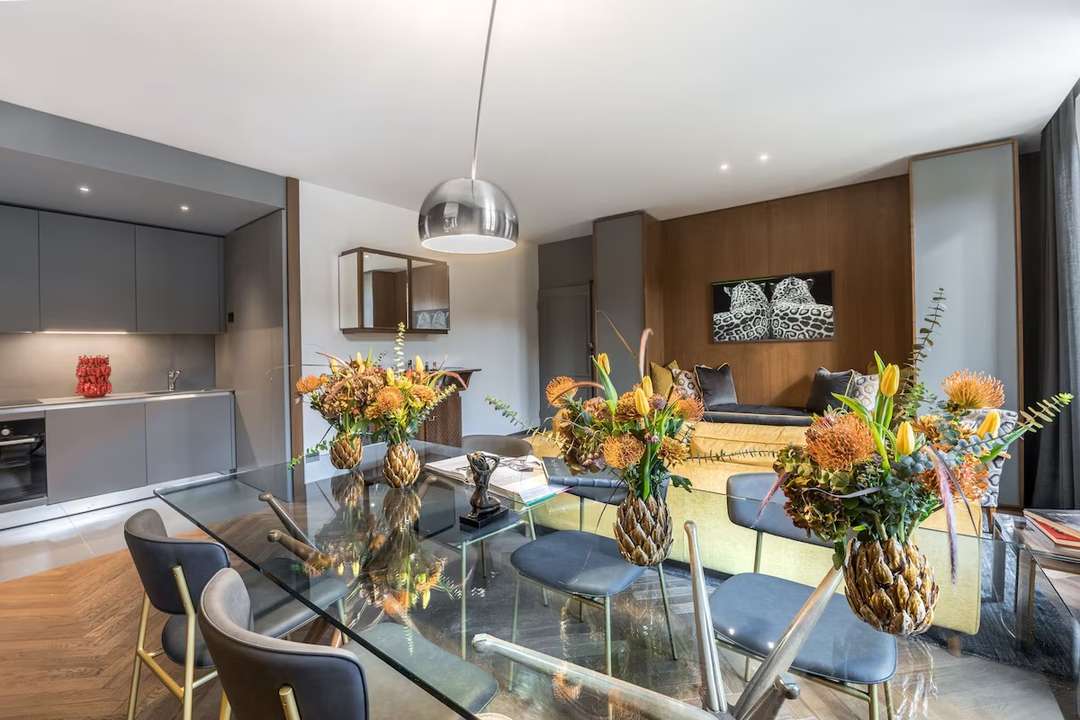 Elegant glass dining table and modern kitchen in Buonadea, a luxury Florence apartment with mid-century design aesthetics.
