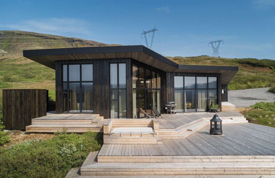 Modern luxury villa exterior in Iceland featuring dark wood siding, expansive windows, and a spacious deck with scenic views.