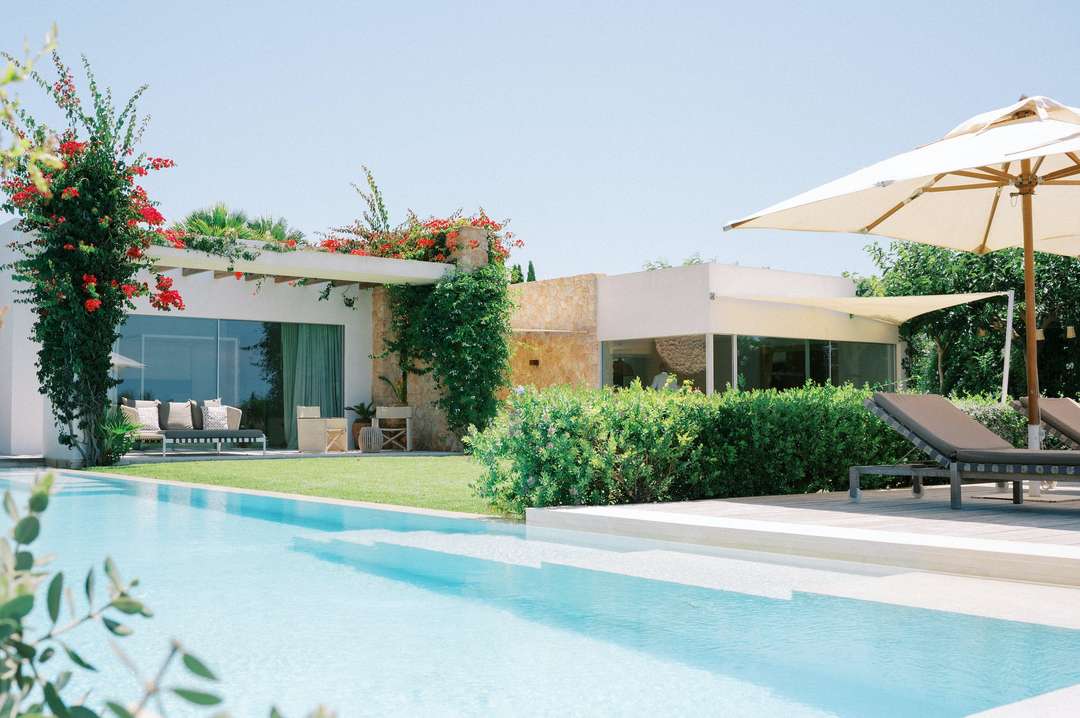 Sun-soaked private pool and terrace at Cala Conta Dream, featuring modern white architecture, stone walls, and lush gardens.