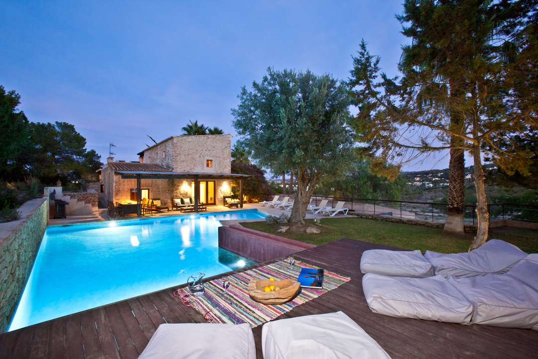 Evening at Can Cala Bassa featuring a private L-shaped pool, wooden deck with beanbags, and traditional stone architecture.