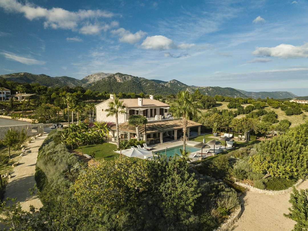 Aerial view of Can Gabriela, a luxury stone villa with a saltwater pool, surrounded by Mallorcan countryside and mountains.