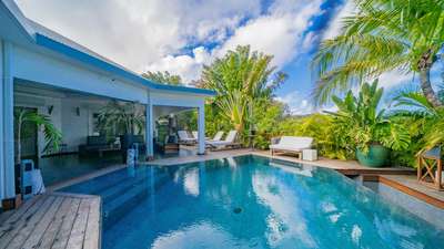 Expansive wooden terrace with a heated hexagonal pool, sun loungers, and tropical gardens offering distant ocean views.