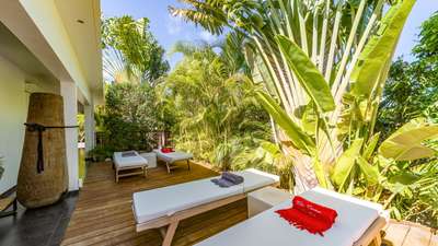 Plush white sun loungers on a spacious wooden deck, enveloped by vibrant tropical gardens at this tranquil St. Barths villa.