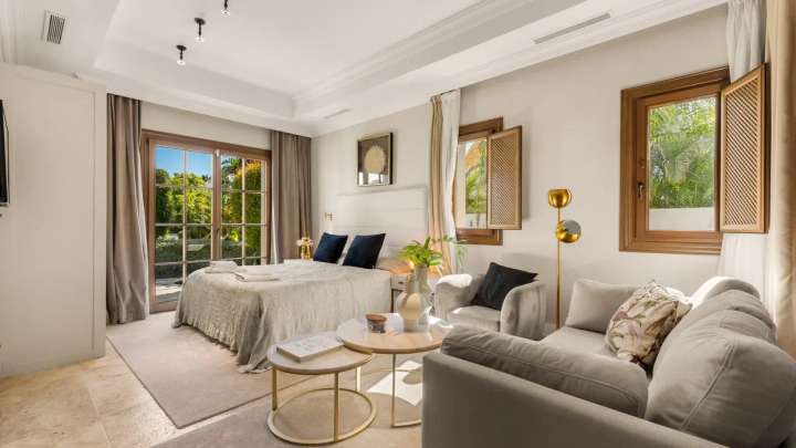 Spacious bedroom with a comfortable double bed, cozy sitting area, and direct access to landscaped gardens in Marbella.