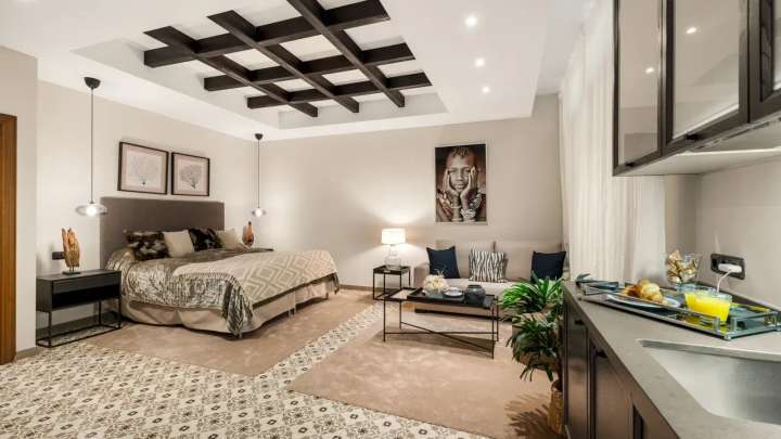 Spacious bedroom suite with exposed wooden beams, a private lounge area, and a sleek kitchenette at Golden Carolina.