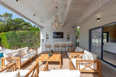 Covered outdoor lounge and bar featuring stylish wooden furniture, mood lighting, and TV at a luxury Algarve villa.