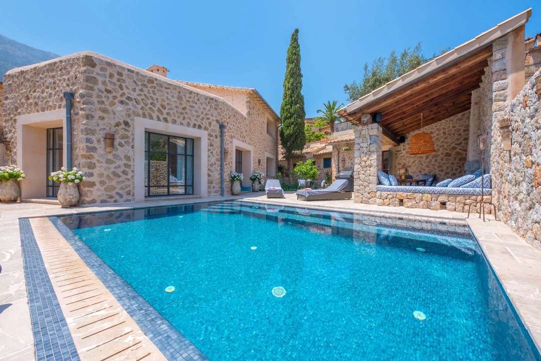 Infinity pool at The Poet's Perch in Deia, featuring a traditional stone facade, contemporary windows and a covered terrace.