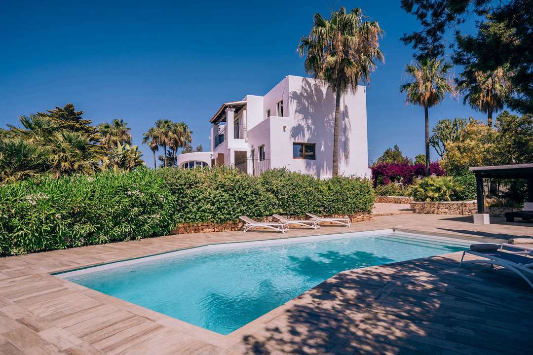 Casa Labonita's stunning white exterior and private pool, surrounded by lush gardens and palm trees under the Ibizan sun.