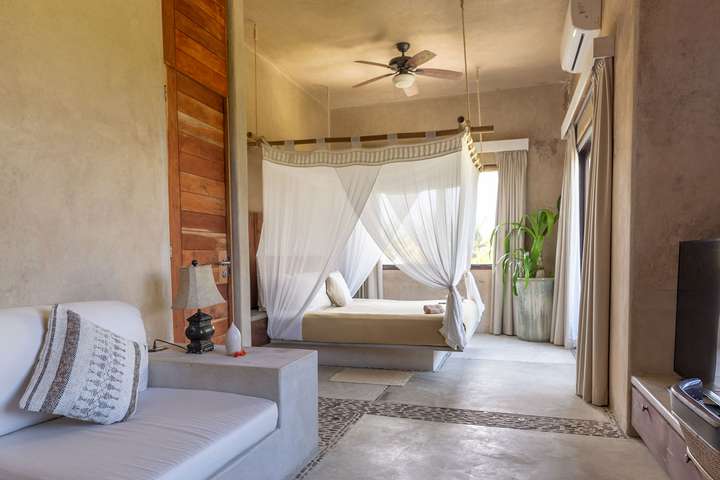 Elegant master suite featuring a king bed with a romantic white canopy and polished concrete floors at Casa Maya Ka'an.