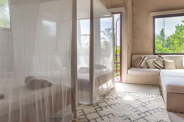 Luxurious Tulum villa bedroom featuring twin canopy beds, rustic-chic design, and a cozy lounge area with tropical views.