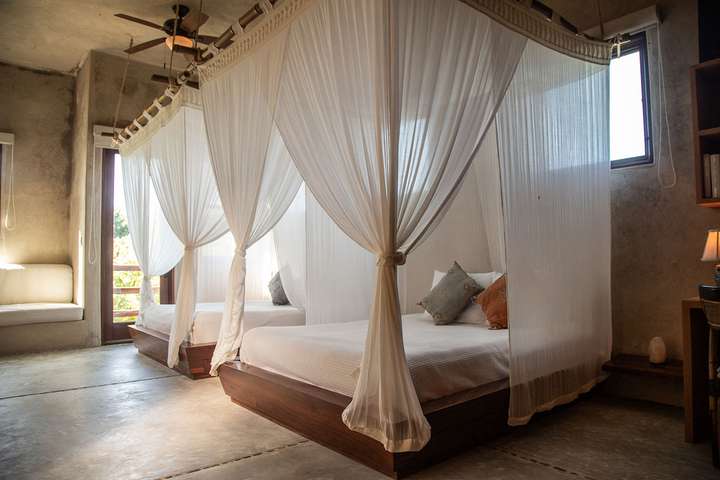 Elegant bedroom suite with twin canopy beds, wooden frames, and polished concrete floors at Casa Maya Ka'an Tulum.