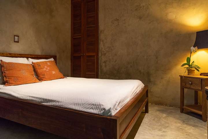 Rustic-chic Tulum bedroom at Casa Maya Ka'an with a wooden bed, vibrant Oaxacan decor accents, and elegant furnishings.
