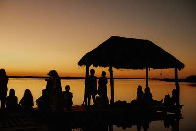 Silhouettes of guests enjoying a tranquil sunset over the emerald Sian Ka'an lagoon from a private deck at Casa Maya Ka'an.