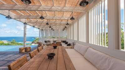 Refined outdoor dining area under a pergola, featuring a wooden table for ten and a serene lounge with panoramic sea views.