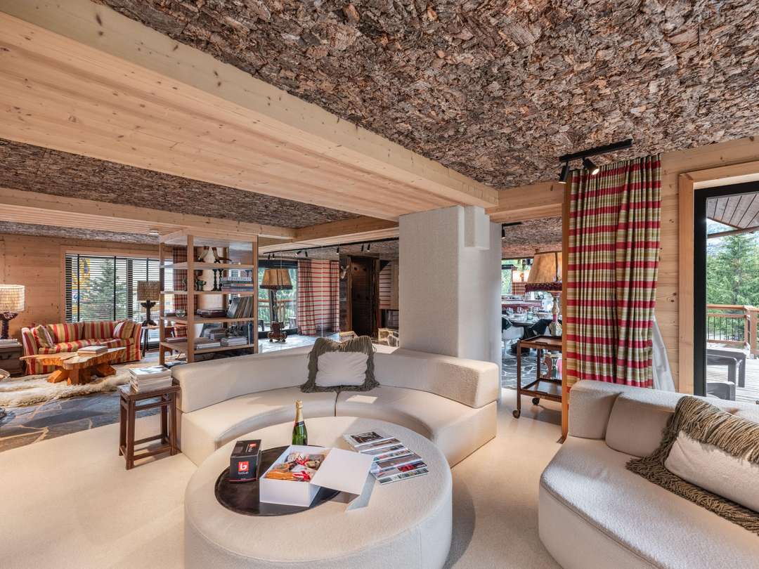Elegant living area at Chalet Coudou Lodge with a curved sofa, unique cork ceiling, stone floors, and scenic mountain views.
