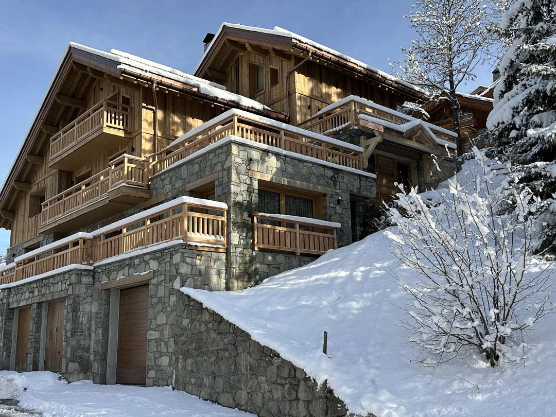 Exterior of luxury Chalet Etoile des Neiges in Meribel, featuring elegant stone and wood architecture in a snowy landscape.