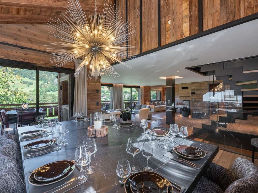 Elegant dining area in Chalet Grizzly featuring a dark marble table, striking starburst chandelier, and scenic mountain views.