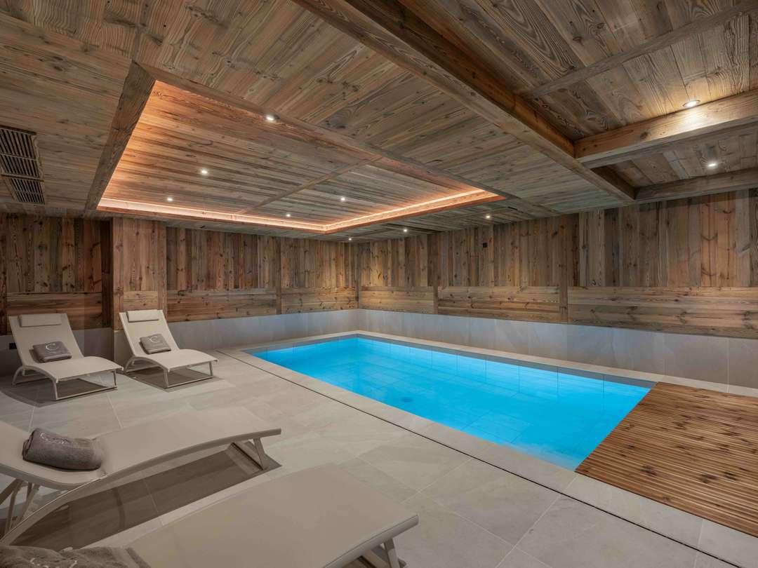 Elegant indoor pool at Chalet Snow featuring warm wood paneling, ambient lighting, and plush loungers for post-ski relaxation.